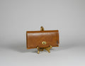 Brown leather clutch on a stand next to stacked books with a plant in the background