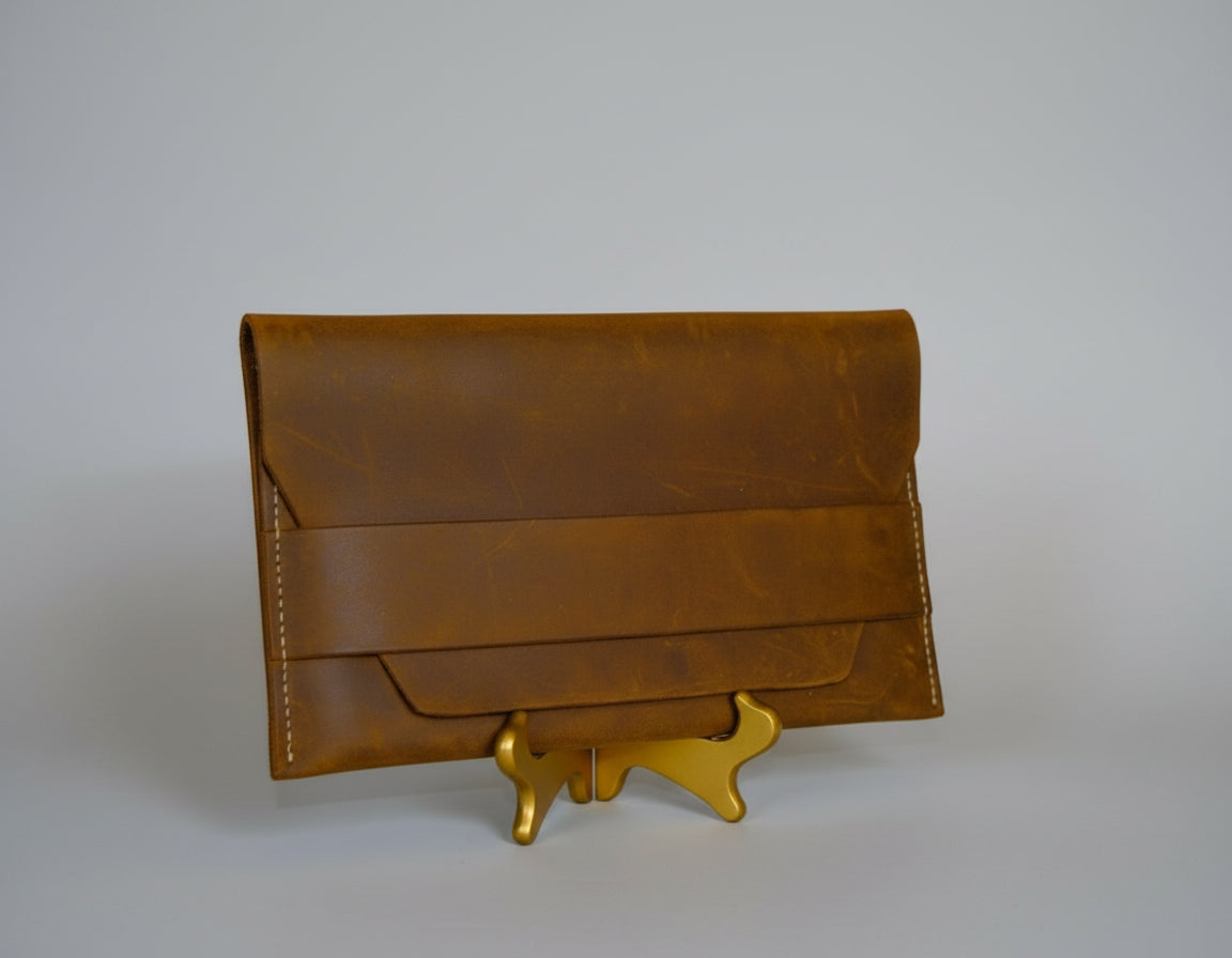 Brown leather clutch on a wooden stand with books and a plant in the background